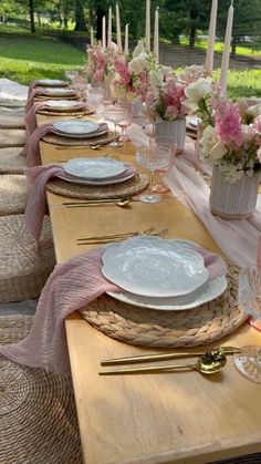 the table is set with pink and white flowers in vases, plates and silverware