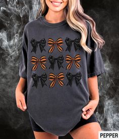 Our Comfort Colors Halloween retro style graphic tee features coquette orange striped and black bows. Our crewneck pairs perfectly with other matching style variations (linked below). ✩ ✩ 𝗔𝗱𝘂𝗹𝘁 𝗖𝗼𝗺𝗳𝗼𝗿𝘁 𝗖𝗼𝗹𝗼𝗿𝘀 𝗧𝗲𝗲: https://starrieapparel.etsy.com/listing/1760615242 ✩ 𝗔𝗱𝘂𝗹𝘁 𝗚𝗶𝗹𝗱𝗮𝗻 𝗦𝘄𝗲𝗮𝘁𝘀𝗵𝗶𝗿𝘁: Halloween Coquette Bows Shirt, Girly Halloween Tshirt, Preppy Cottagecore Graphic Tee Spooky Girl Aesthetic Comfort Colors Plus Size T-shirt SIZE UP for an OVERSIZED FIT (see size chart in listing photos). ✩ Our shop uses direct-to-garment printing to make our products. The design ink is sprayed on, then allowed to soak into the fibers of the garment. This process yields fine quality prints and a smooth finish on the garment. 𝗖𝗢𝗠𝗙𝗢𝗥𝗧 𝗖𝗢𝗟𝗢𝗥𝗦® Garment Retro Black T-shirt For Fall, Black Retro T-shirt For Fall, Spooky Girl Aesthetic, Preppy Cottagecore, Halloween Coquette, Girly Halloween, Black Bows, Coquette Bows, Halloween Retro