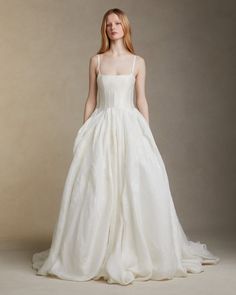 a woman in a white wedding dress standing on a gray background with her hands behind her back