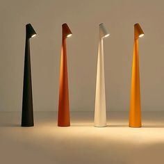 four different colored lamps are standing in a row on the floor with one light turned on