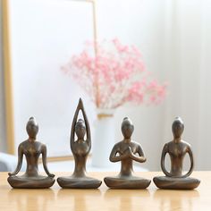 three figurines sitting on top of a wooden table next to a vase with pink flowers