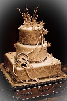 a three tiered wedding cake with a clock on the top and pearls around it