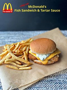 a chicken sandwich with cheese and fries on a piece of wax paper next to it