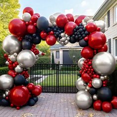 an arch made out of balloons in front of a house on a brick walkway with a black gate