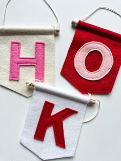 three felt banners with the letters k and h hanging from strings on a white surface