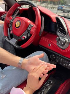 a woman driving a red sports car with her hand on the steering wheel