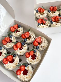 cupcakes with strawberries and blueberries are in a box on the table