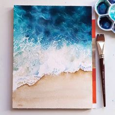 an artist's palette and watercolors on a white table with a blue ocean painting