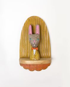 a wooden sculpture of a rabbit wearing a suit and bow tie, on a shelf