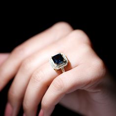 a woman's hand holding a ring with a blue and white diamond on it