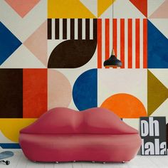 a pink couch sitting in front of a wall with colorful geometric designs on the walls