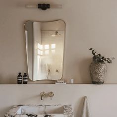 a bathroom sink sitting under a mirror next to a vase with flowers on top of it