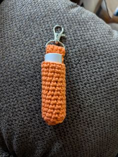 an orange crochet keychain hanging from the back of a person's arm