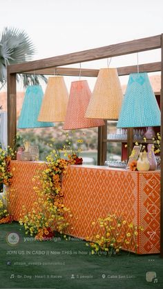 an orange and blue table with lamps hanging from it's sides in front of a palm tree