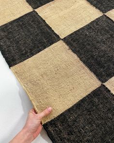 a hand is pointing at a black and white checkered rug