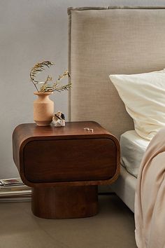 a bed with a wooden night stand on top of it next to a white pillow