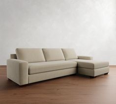 a beige couch sitting on top of a wooden floor next to a white wall in an empty room