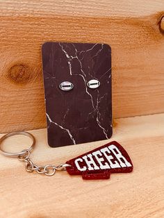 a piece of wood that has some type of keychain attached to it, with the word cheer on it