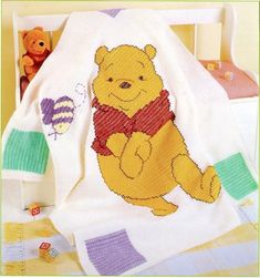 a crocheted winnie the pooh blanket and stuffed animal on a bed with other items