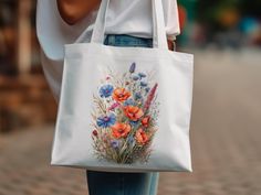 "Step out in style with our \"Summer Blossom Watercolor Tote,\" where functionality meets the splendor of summer gardens. Adorned with a lush display of wildflowers, this tote showcases stunning watercolor artistry with poppies and cornflowers in vivid shades of orange, pink, and blue. Each brushstroke celebrates the delicate textures and gradients only achievable with watercolor techniques, giving life to this 100% cotton canvas tote. The robust self-fabric handles provide comfort and resilience for daily use, while the generous 15\"x16\" size ensures you have ample space for your essentials. Printed using state-of-the-art Direct-to-Garment technology, the colors remain radiant wash after wash, making this bag a durable piece of art. Perfect for those who value eco-friendly fashion, this Summer Gardens, Blossom Watercolor, Flower Tote Bag, Flower Tote, Minimalist Shirts, Small Acts Of Kindness, Eco Friendly Fashion, Flower Shirt, Wild Flower