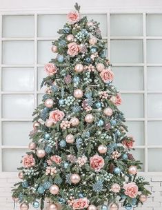 a decorated christmas tree in front of a window with pink and blue ornaments on it