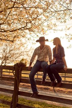 a man and woman sitting on a bench in front of a tree with the sun behind them