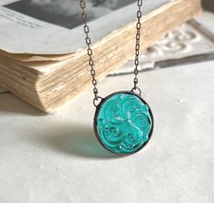 "Teal colored pressed glass pendant measuring almost 1 1/2\", with a flat back, is soldered and finished with an antiqued patina.  This simple yet interesting round glass pendant hangs from a 18\" antiqued brass chain with lobster clasp.  You can choose your own personal chain length at check out. You can also choose bib (shown) chain style, or traditional (one attached hook). View more  necklaces here - https://www.etsy.com/shop/ThatOldBlueHouse2?section_id=18312372&ref=shopsection_leftnav_5" Stain Glass Jewelry, Vintage Glass Pendant Necklace, Blue Glass Necklace, Antique Handmade Glass Necklaces, Stained Glass Necklace Pendant, Unique Glass Necklace Pendant Folksy, Stained Glass Necklace, Teal Necklace, Elven Jewelry