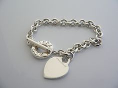 Overview:Offered for sale is a wonderful and gorgeous Tiffany & Co. Sterling Silver Heart Toggle bracelet. Definitely a Tiffany piece that you will get your money's value for. It works perfectly with pretty much any attire your put on, AND is a great statement piece. The chain for this specific bracelet very substantial, and the pretty Tiffany heart just goes perfectly with it. It is the perfect bracelet that fits a lifestyle on the go -- can be worn to pretty much any occasion! It is simple Elegant Heart Bracelet With Toggle Clasp For Valentine's Day, Designer Silver Jewelry With Heart Charm, Elegant Valentine's Day Bracelets With Toggle Clasp, Elegant Heart Bracelet With Toggle Clasp For Gift, Heart-shaped Jewelry With Clasp For Gifts, Heart-shaped Jewelry Gift With Clasp, White Gold Jewelry With Clasp For Gift, Elegant Charm Bracelet With Toggle Clasp As Gift, Classic Bracelets With Toggle Clasp As Gift