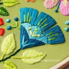 a close up of a embroidery on a piece of cloth with flowers and leaves around it