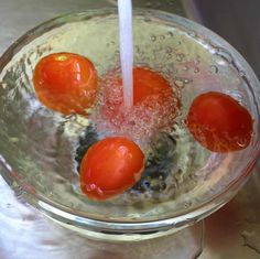 tomatoes are being washed in a glass bowl