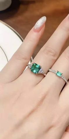 a woman's hand with two rings on top of her finger and an emerald stone in the middle