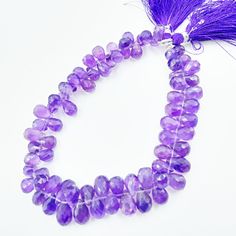 a purple necklace with tassels and beads on a white surface, next to a purple feather