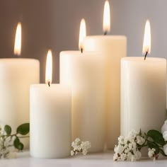 white candles are lined up next to flowers