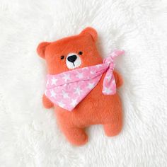 a brown teddy bear with a pink bandanna around it's neck on a white blanket