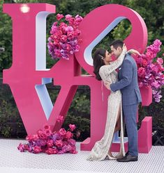 a man and woman kissing in front of a large love sign with flowers on it