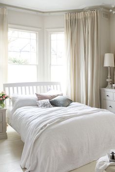 a white bed sitting in a bedroom next to two windows