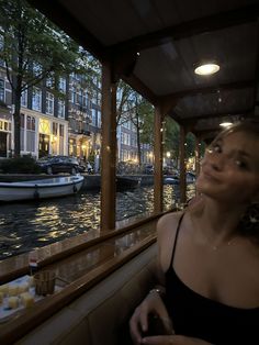 a woman sitting at a table in front of a river with boats on the water