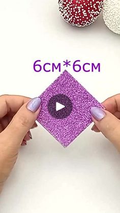 two hands are holding an ornament with purple glitter