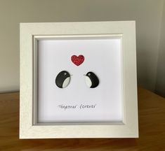 two black and white birds with red hearts on their backs in a white shadow box frame