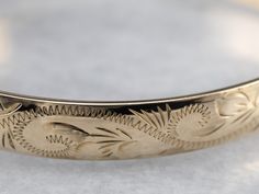 This vintage bangle bracelet is gorgeous and so versatile! Crafted of 10 karat gold, this piece has a nice weight to it and is adorned with gracefully engraved botanical motifs. The hinged design and safety chain add practicality and wearability without compromising style. Metal: 10K Yellow Gold Width: 8 mm Inside Circumference: 7 Inches Marks: "10K" Stamped on the clasp Heirloom Yellow Gold Cuff Bracelet For Ceremonial Occasions, Ceremonial Heirloom Yellow Gold Cuff Bracelet, Vintage Yellow Gold Cuff Bracelet With Intricate Design, Traditional Engraved 14k Gold Bracelet, Traditional 14k Gold Engraved Bracelet, Antique Engraved Yellow Gold Cuff Bracelet, Antique Etched Yellow Gold Bracelets, Antique 14k Gold Bangle, Antique Yellow Gold Cuff Bracelet For Ceremonial Occasions