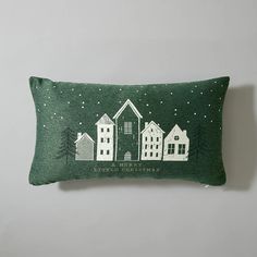 a green pillow with white houses and trees on it, against a gray background that has snow falling from the sky