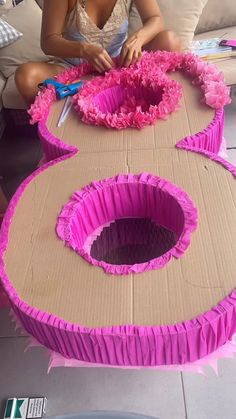 a woman is sitting on the floor making pink paper flowers