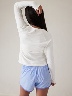 a woman with her back to the camera wearing blue shorts and a white top, standing in front of a wall