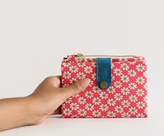 a hand holding onto a small pink and white flowered purse with a blue strap