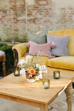 a wooden table topped with vases filled with flowers next to a couch and chair