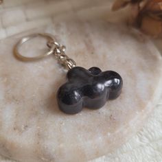 a black cloud shaped keychain sitting on top of a white marble slab with pine cones in the background