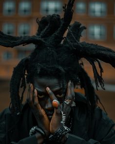 a man with dreadlocks covers his face while holding his hands to his face