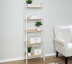 a white chair sitting next to a book shelf with plants on it and boxes in front of the shelves