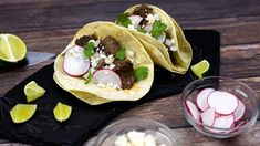 two tacos with meat, radishes and cilantro on a black plate