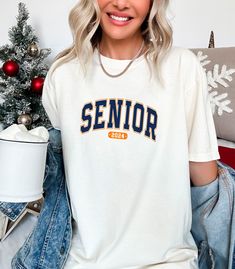 a woman sitting on a couch wearing a white shirt with the word senior printed on it